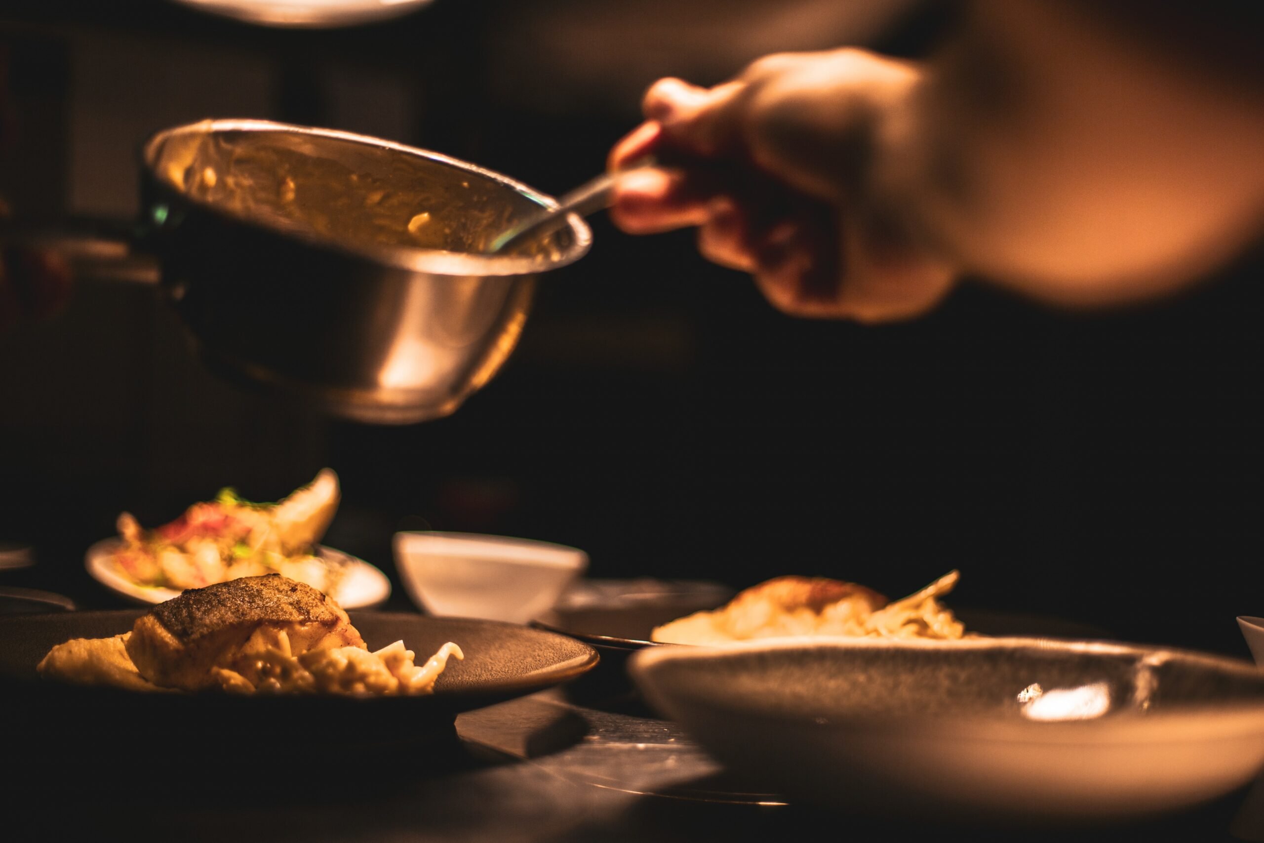 A person prepares to drizzle sauce over a dish of meat